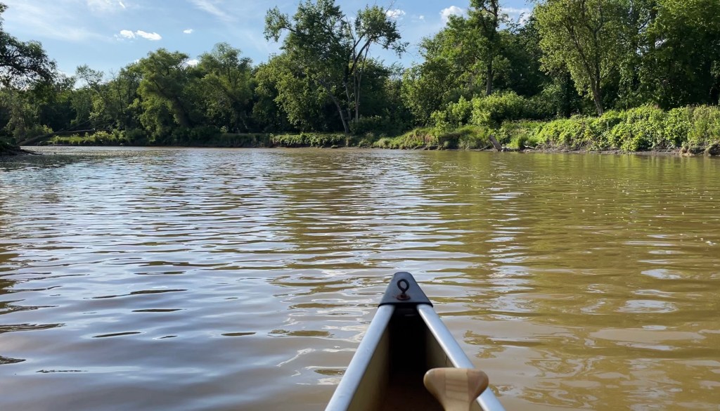 The front of a canoe on a gently flowing river on a sunny day