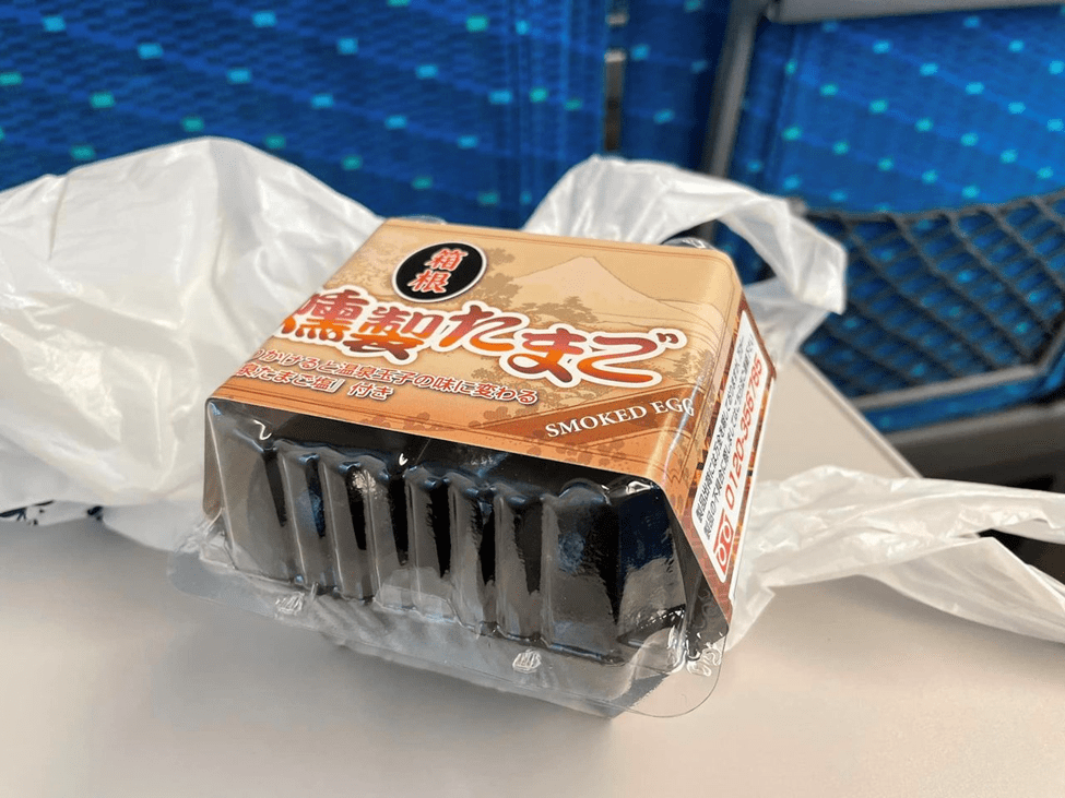 A plastic pack of smoked eggs, labeled in Japanese, sitting on a bullet train tray